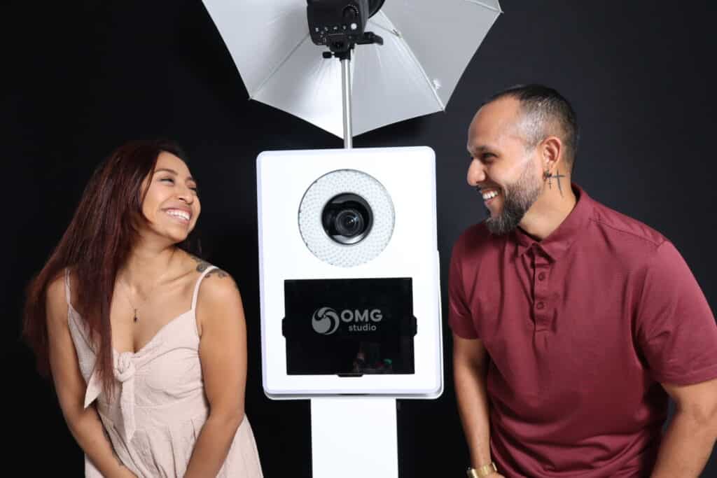Couple smiling in front of a photo booth with OMG Studio branding, showcasing interactive photo experiences ideal for engaging audiences at events in Wynwood.