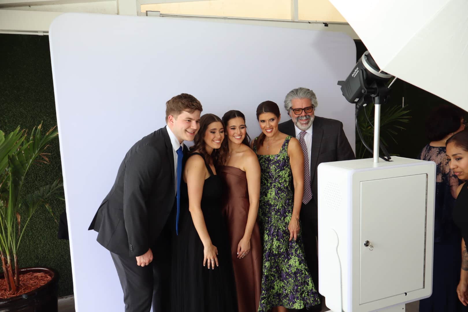 Group of five people posing together at a wedding photo booth, featuring a sleek photo booth setup, vibrant dresses, and a joyful atmosphere, highlighting guest engagement and memorable moments.