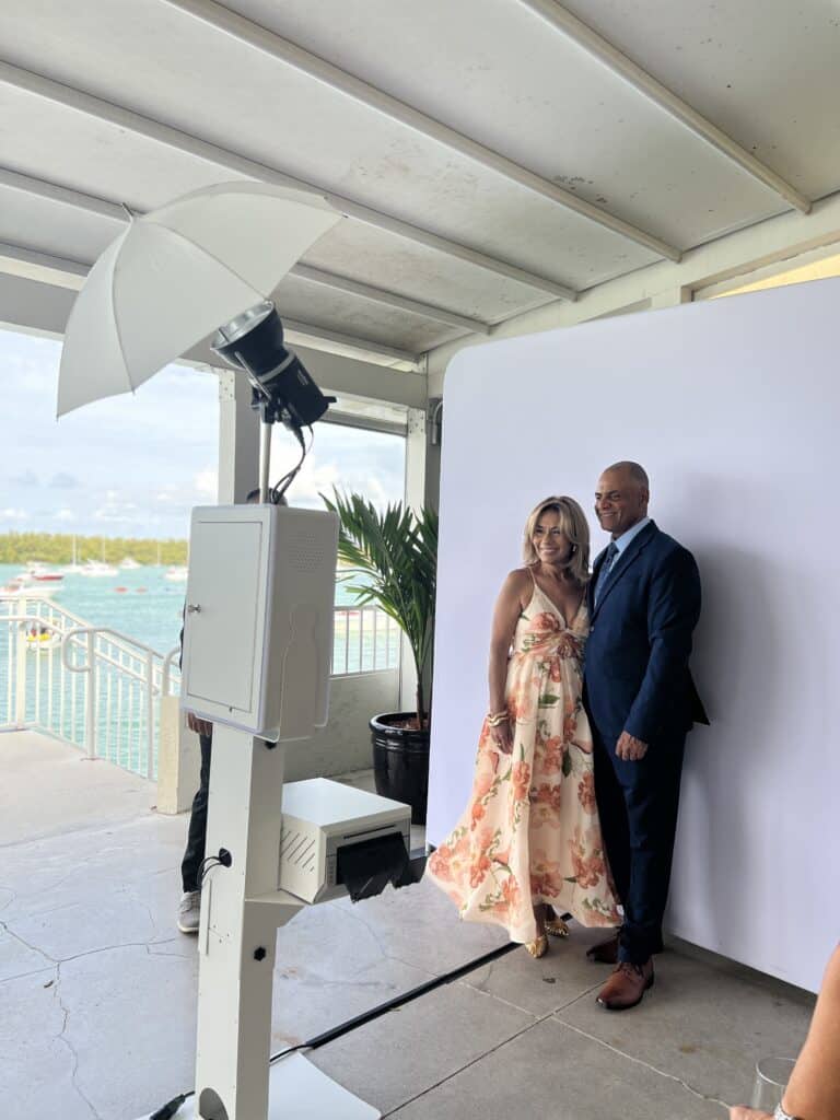Couple posing in front of a Glam Booth with a white backdrop and lighting setup, showcasing a photo experience at an event by OMG Studio.