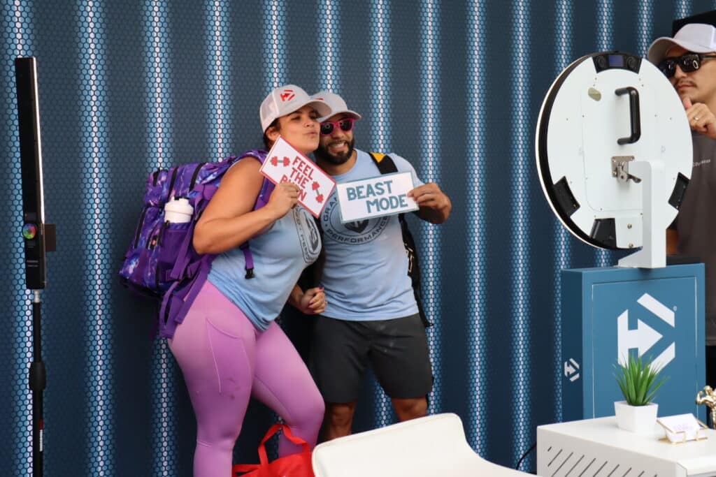 Couple posing with playful signs "FEEL THE BURN" and "BEAST MODE" at a roaming photo booth, showcasing candid engagement and vibrant event atmosphere in Miami.